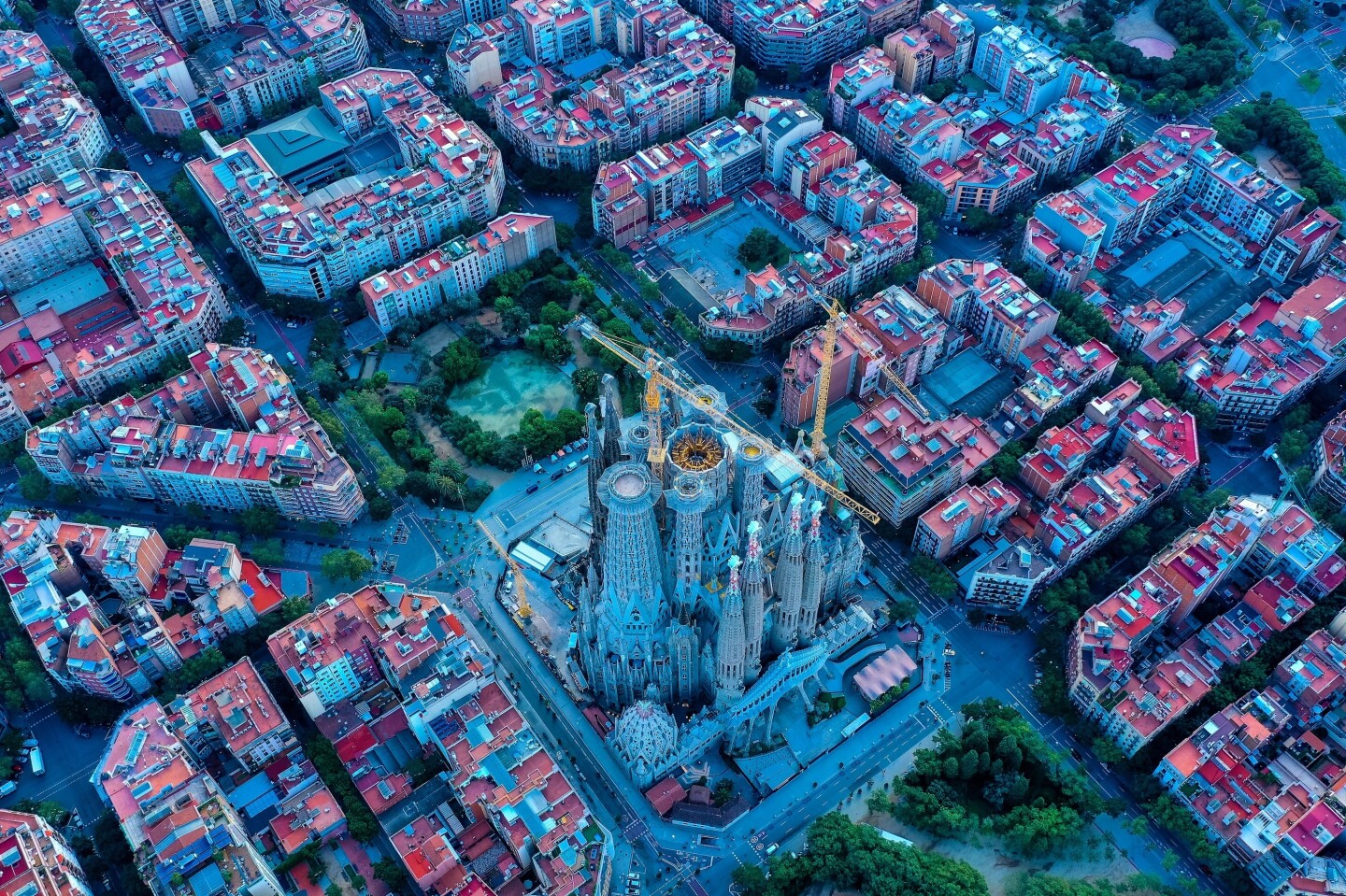 Bird's-eye view of the Sagrada Familia in Barcelona, with predominantly red rooftops of apartment buildings and businesses surrounding it