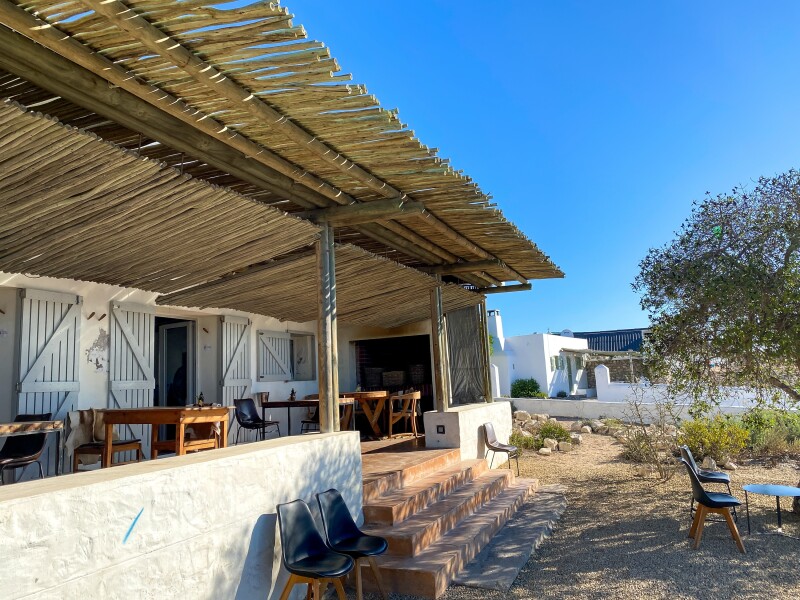 View of veranda seating at Wolfgat Restaurant, a simple structure with a roof made from reeds