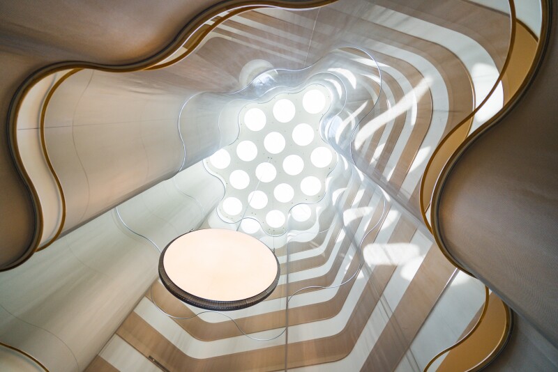 A view looking skyward at a curvy, wiggly-edged atrium with circular skylights at the top