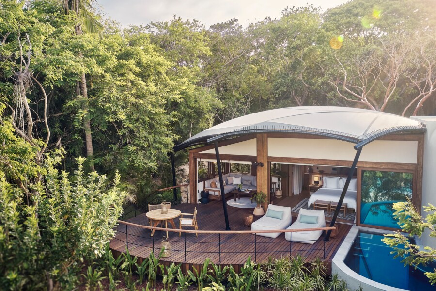 Tented hotel room, with plunge pool and wooden deck with two white lounge chairs surrounded by jungle