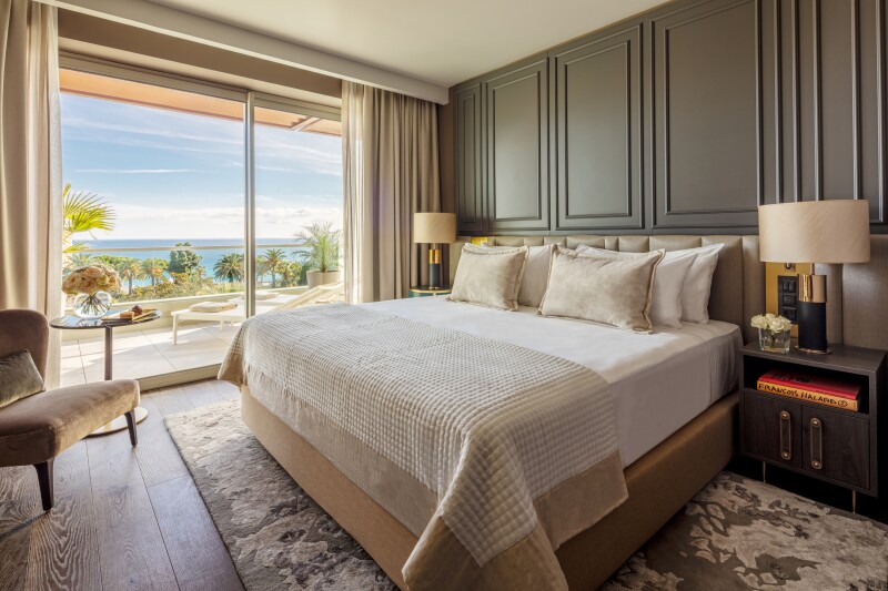 A guest room at Anantara Plaza Nice Hotel, with neutral palette and floor-to-ceiling glass door to private veranda facing sea