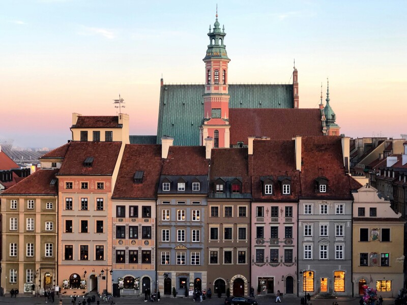 A sunset view of section of Warsaw's Old Town, with row of historic buildings in different pastels and a pink church tower behind them