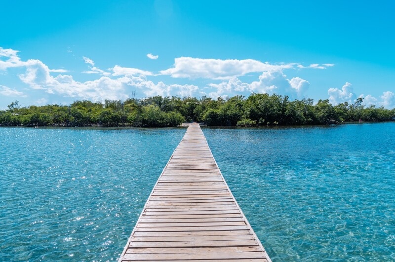 A long wooden boardwalk stretches to small green island at Cayo Aurora