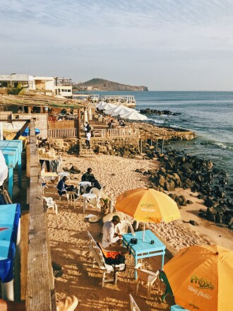 People sitting on chairs on the beach under yellow and orange umbrellas