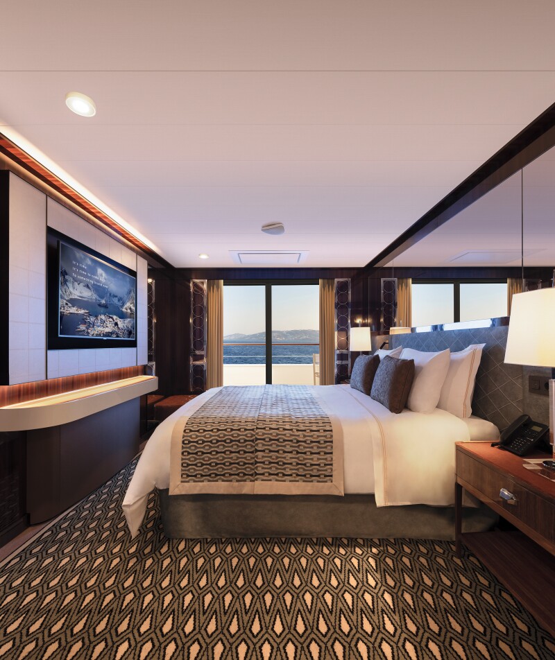 Journey suite with bed, brown and tan patterned carpeting, and glass doors to balcony aboard Atlas Ocean Voyages