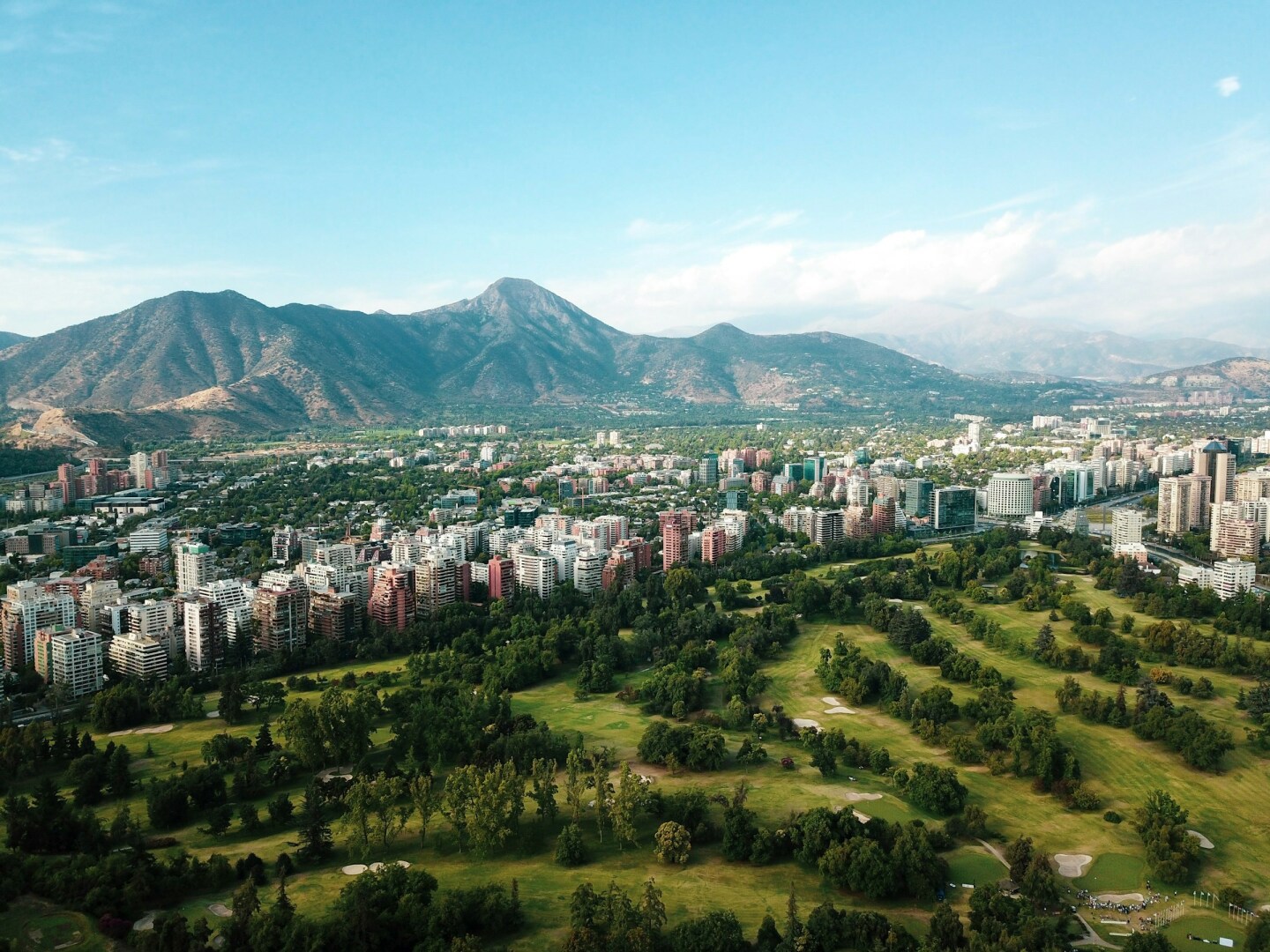 A high view of a golf course and the town and the city and green mountains behind it in in Santiago, Chile.