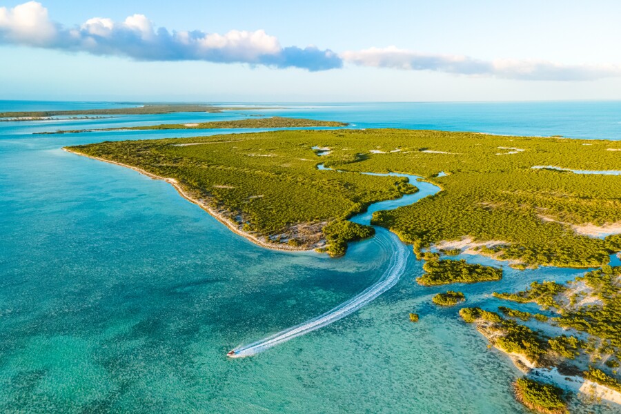 Aerial view of Jet Ski exiting green mangrove channel into shallow Caribbean sea