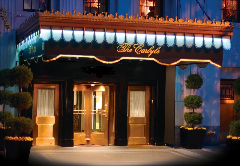 Entrance to the Carlyle at twilight, with illuminated awning and revolving doors