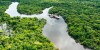An aerial view of the Amazon River in Peru winding through lush green rainforests with a couple boats creating ripples in the water and a small grouping of homes jutting out over the water
