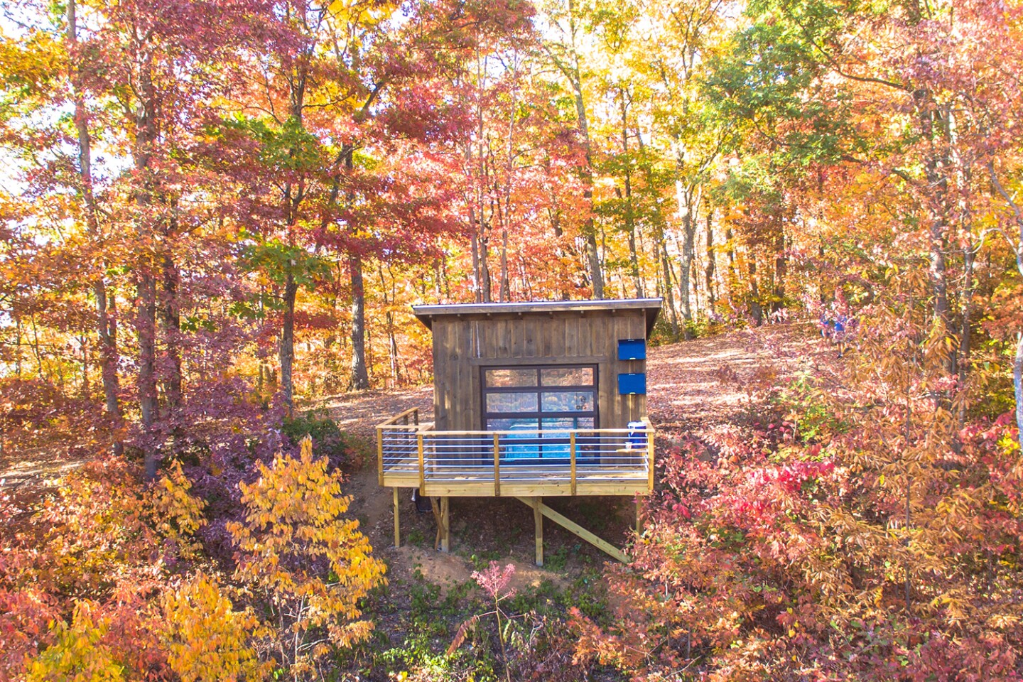 Exterior of small cabin with porch, surrounded by trees in fall colors