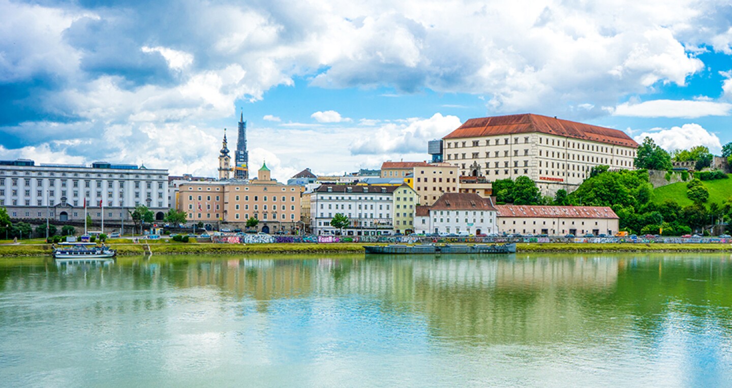Buildings and a cloudy blue sky reflecting on the river in the town of Linz, Austria