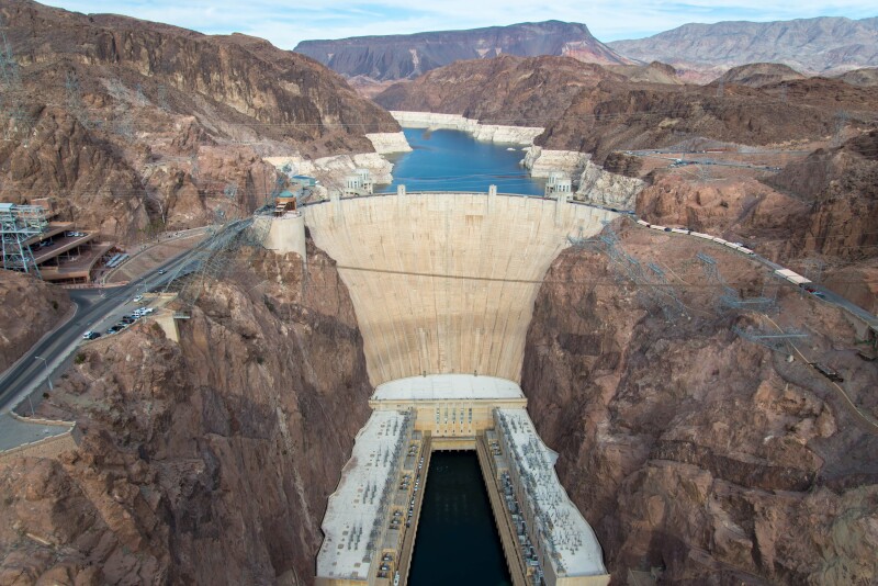 Aerial view of Hoover dam, with part of Lake Mead in distance among rugged brown hills
