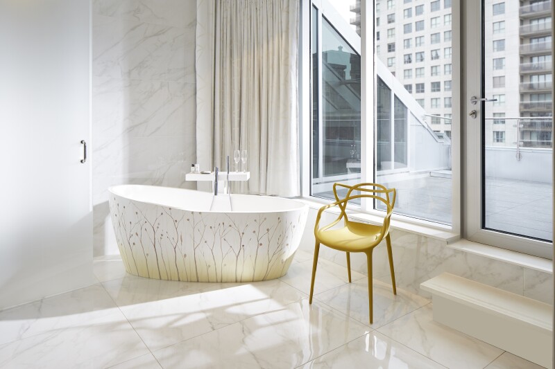 A marble-tiled bathroom with a standalone bathtub decorated with botanical motifs next to a decorative gold chair