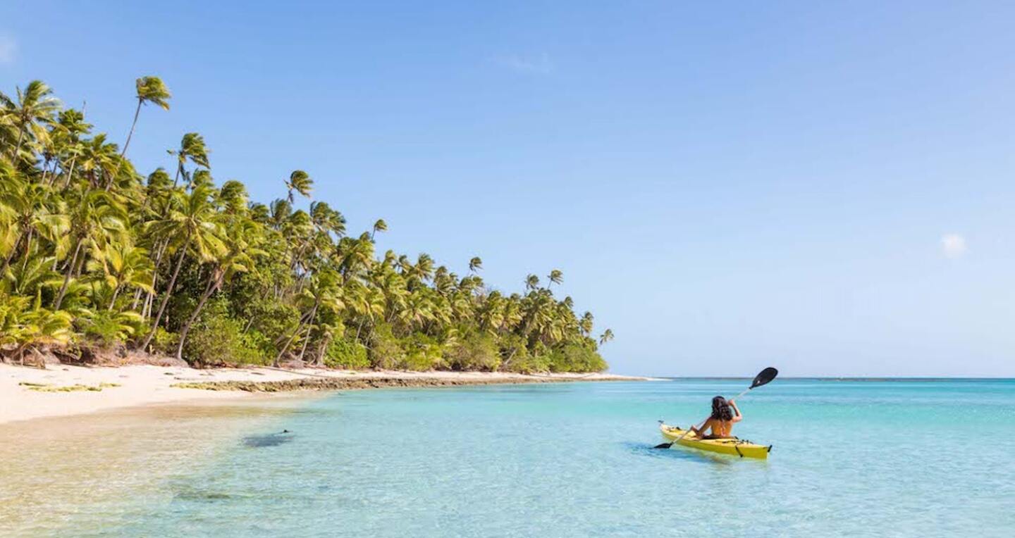 A woman kayaks along the shore of a lush island