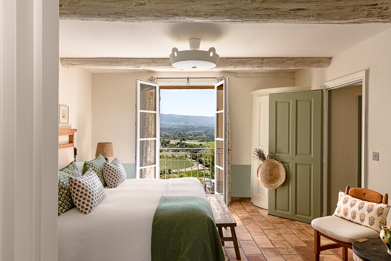 Interior of beige and green guest room with French windows open to green countryside at Hôtel Crillon le Brave