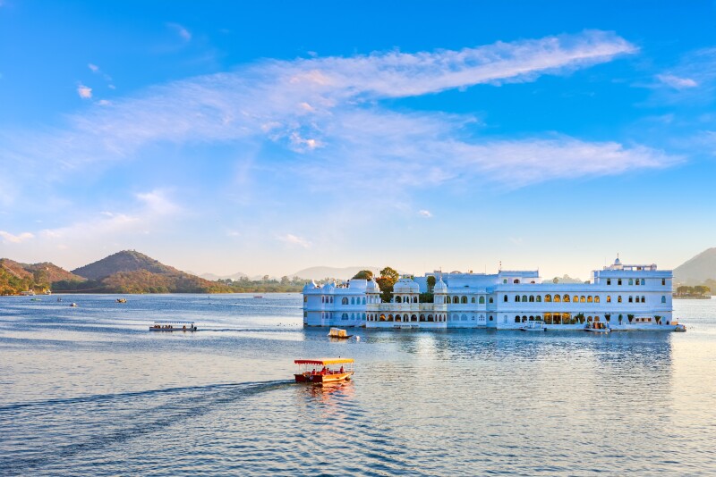 Distant view of white palace in India floating on a lake, with small boat in foreground
