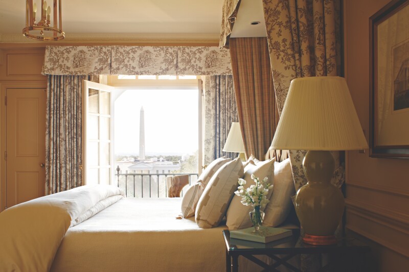 A guest room at the Hay-Adams hotel with a canopy bed, and heavy floral curtains hanging over the door to the balcony, which overlooks the White House and the Washington Monument