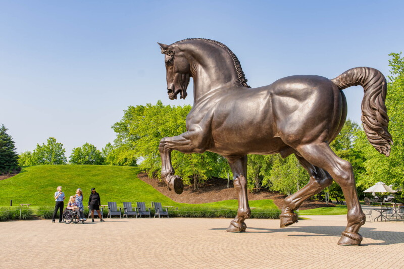 Four people, one in a wheelchair, look up at Nina Akamu’s enormous bronze American Horse sculpture at the Frederik Meijer Gardens and Sculpture Park