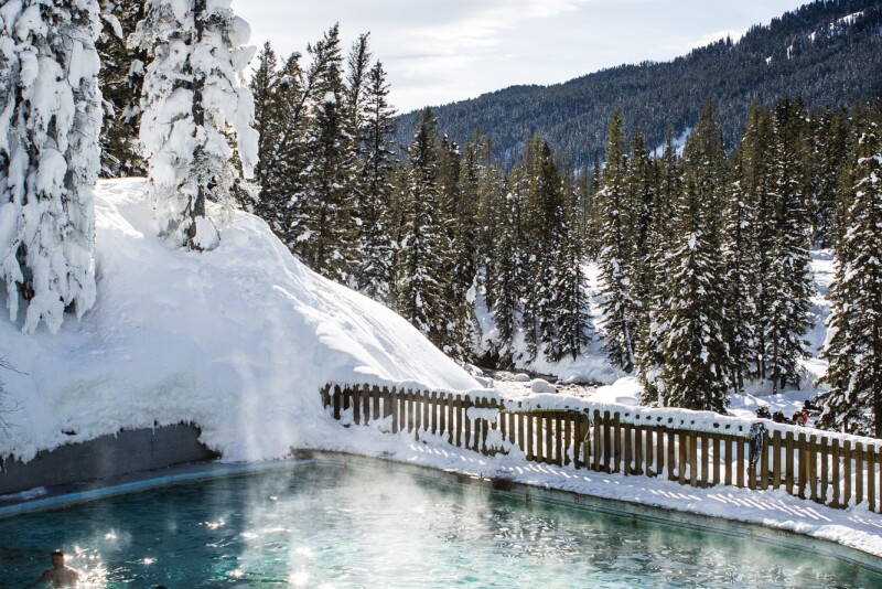A hot spring pool backed by snow-covered evergreen trees and a mountain