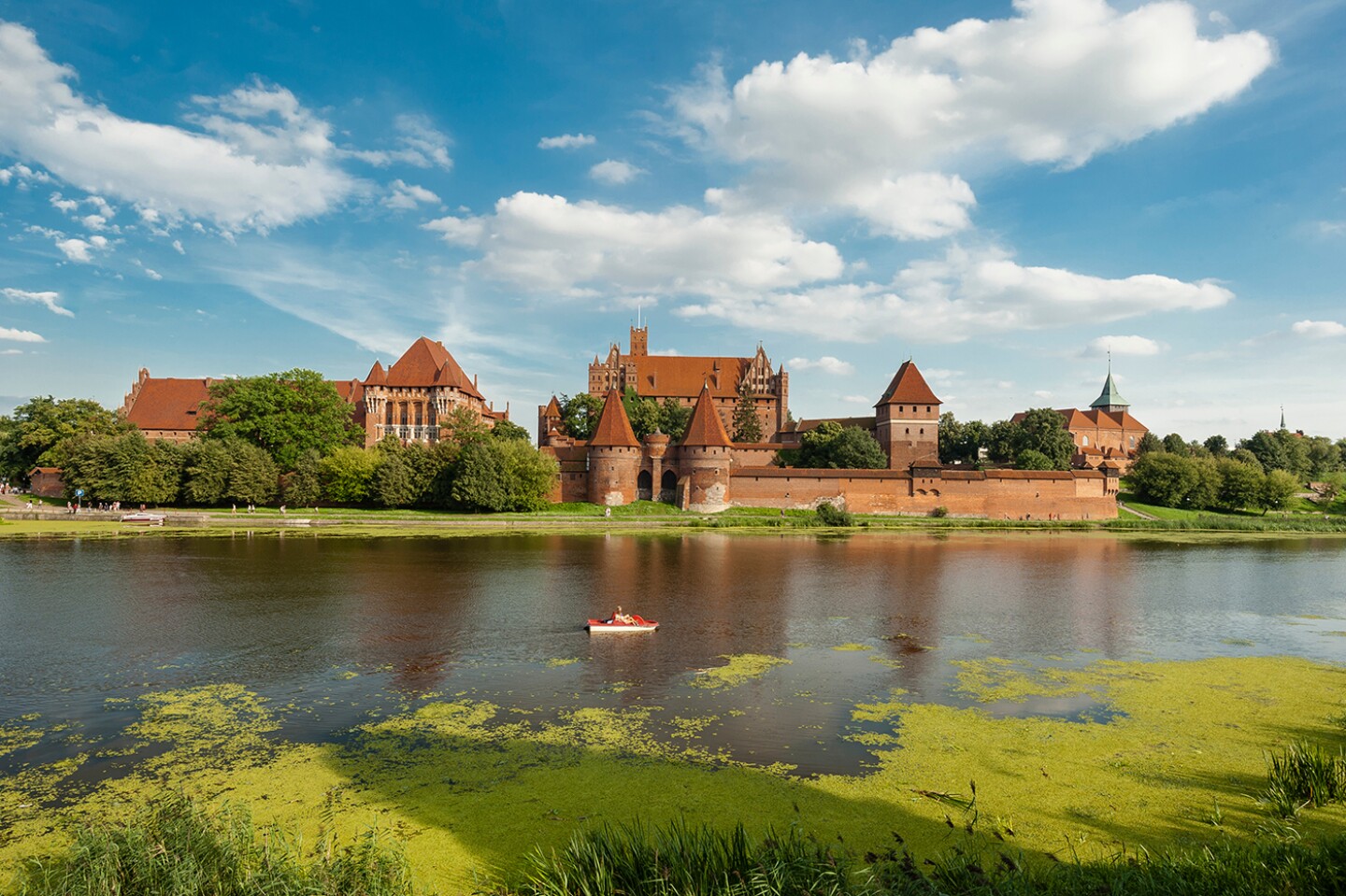 View from river of Poland’s huge, brick, red-roofed Malbork Castle