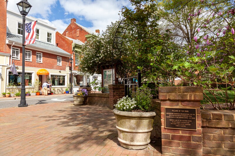Brick sidewalk beside a park, with red brick buildings in background
