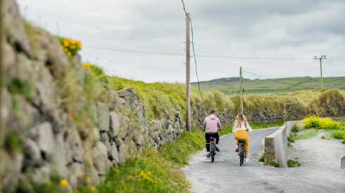 Two tourists riding electric bikes on Inishmore, the largest of the Aran Islands in Galway Bay, Ireland. Renting a bicycle is one of the most popular way to get around Inis Mor.