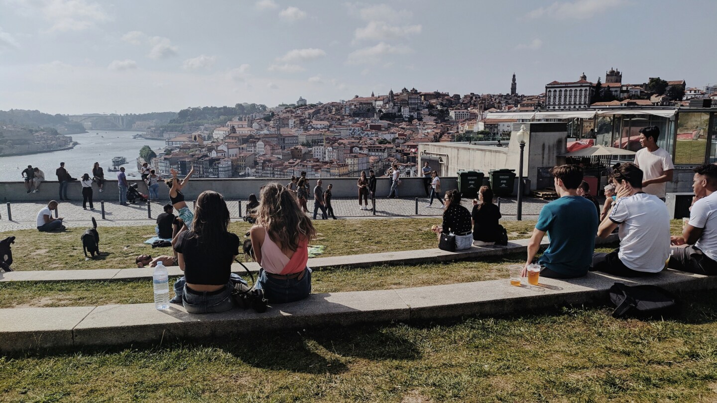 view of the waterfront in Porto, Portugal, as seen from a tiered park with people sitting and playing on the steps and grass