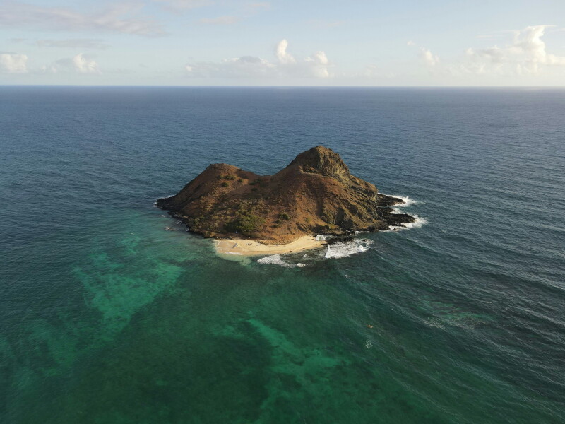 Aerial view of rugged twin-peaked volcanic islet with small sandy beach