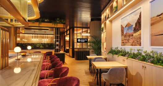 Chase Sapphire Lounge by The Club at Phoenix Sky Harbor International Airport featuring a row of red velvet chairs lining a counter with some two-top dining tables, photos on the walls and plants accenting the art-deco style space