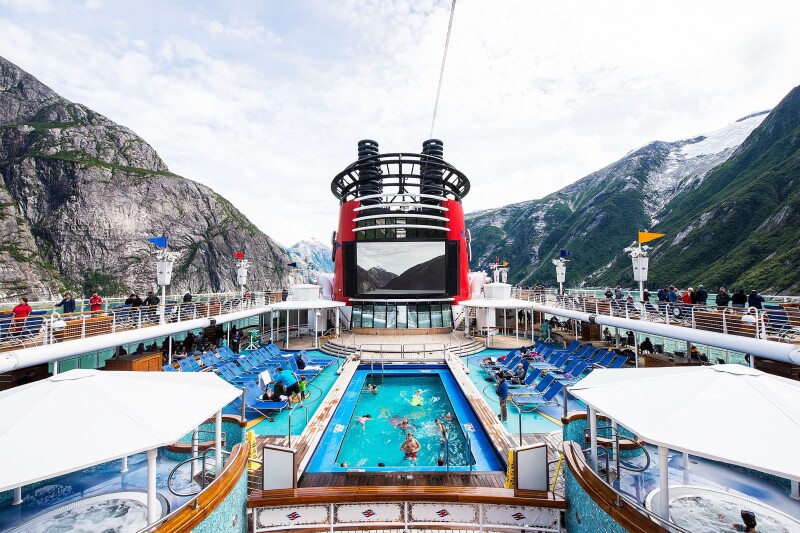 The roof deck of a Disney Cruise Line ship with a swimming pool, hot tubs, and lounge chairs.