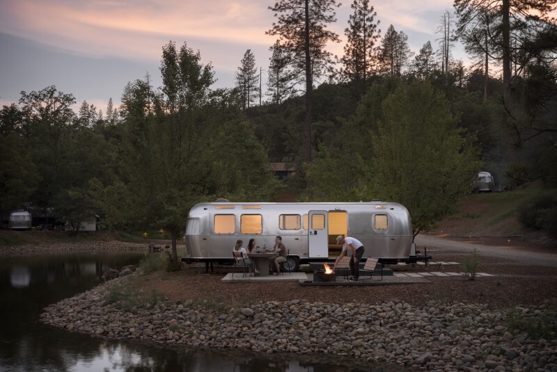 An Airstream trailer at AutoCamp Yosemite surrounded by trees, with outdoor chairs