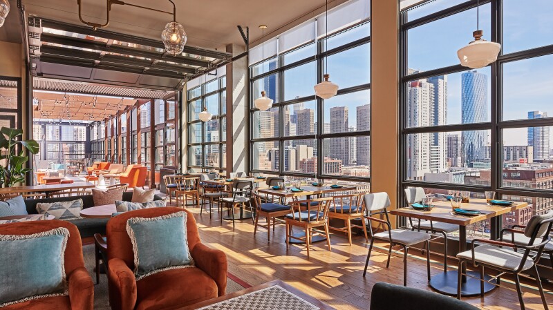 Cabra restaurant with dining tables for four along wall of windows, overlooking downtown