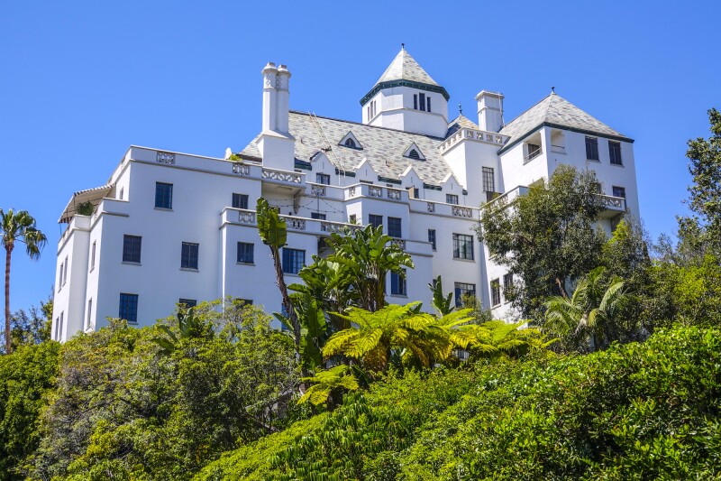 White Chateau Marmont atop hill, viewed from below and surrounded by greenery