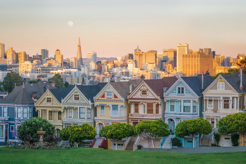 Colorful row of Victorian houses, with modern downtown buildings in background in late afternoon light