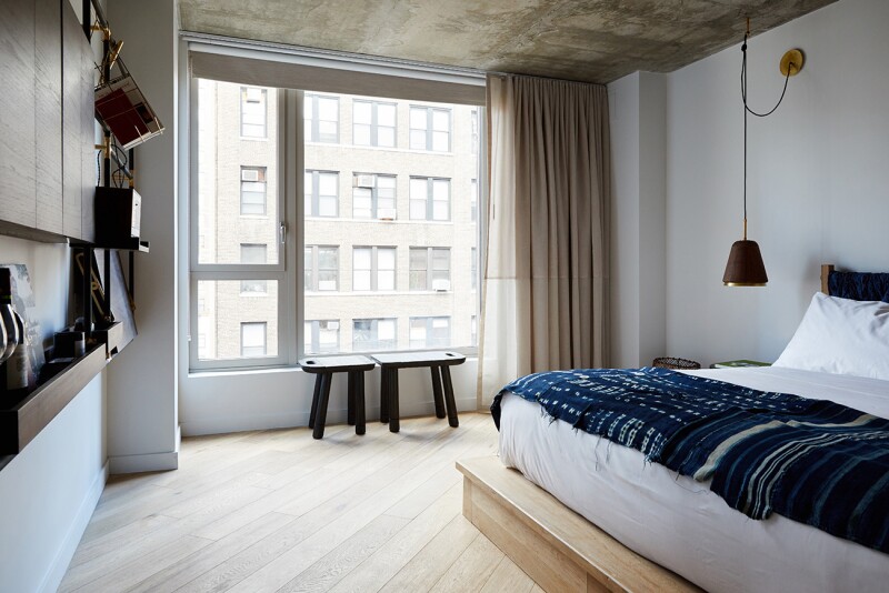Interior of guest room at the Made Hotel, with bronze shelves and small hand-carved benches next to large window