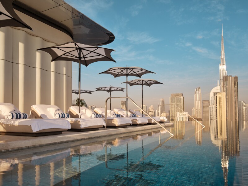 The pool at the Lana, Dorchester Collection, in Dubai features skyline fews and white daybeds shaded by umbrellas.