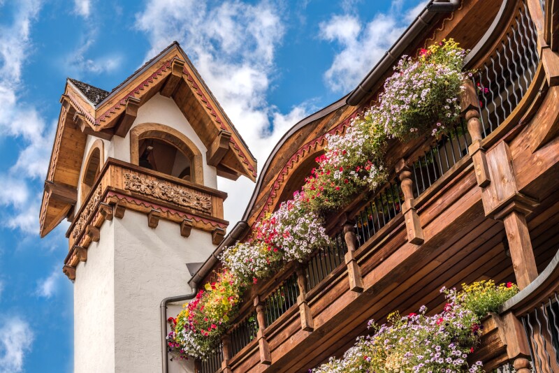 A Bavarian-style building with bell tower and baskets of flowers along wooden porch