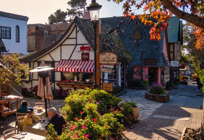 A fairy tale like building with straw roof  houses a small store and people having lunch on a  terrace