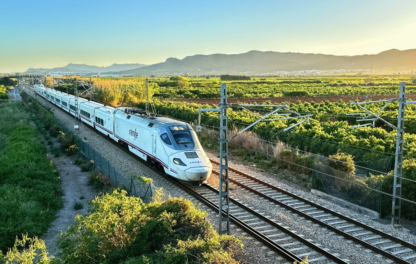 A high-speed train traveling through a green agricultural area of Spain