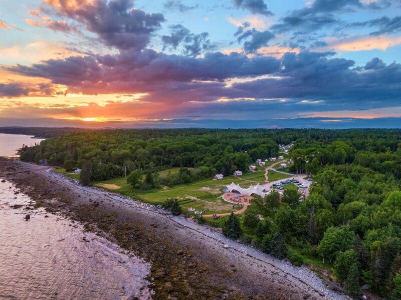 Aerial view of distant tents along a path surrounded by trees near the coast