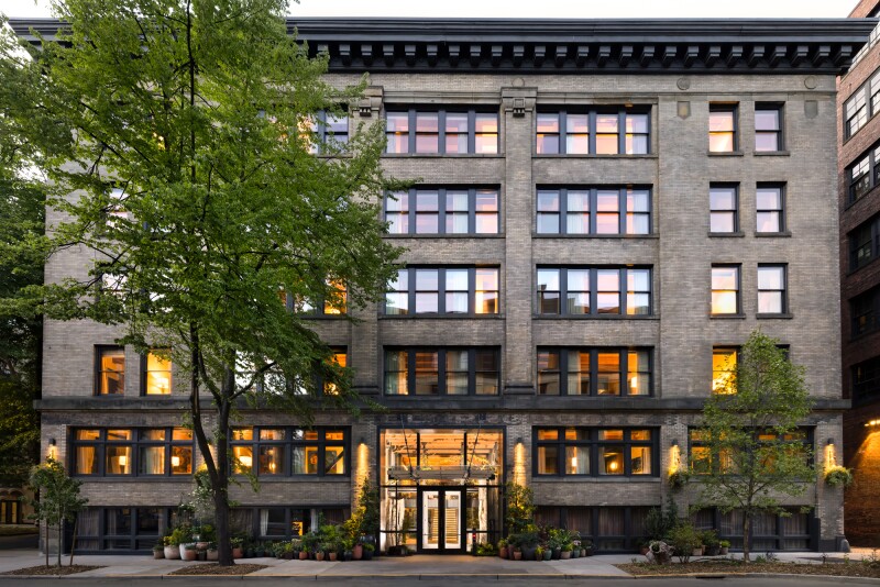 The gray five-story exterior of Populus Seattle, with large tree at left