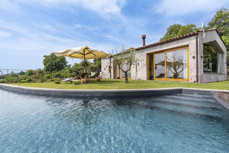 This villa at Monaci delle Terre Nere sits next to a large pool flanked by lounge chairs.
