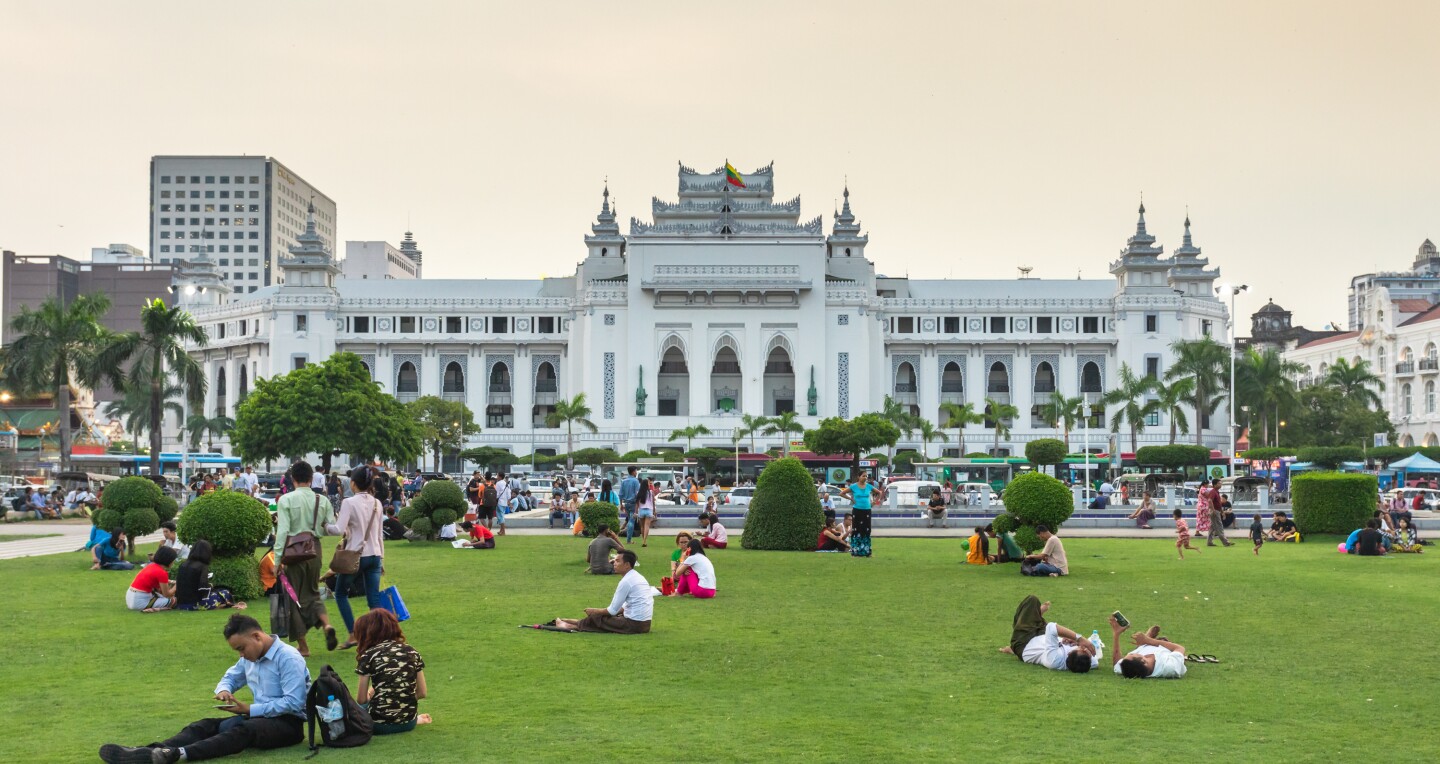 Yangon, Myanmar - 16.05.2019: People sitting on grass in Maha Bandula park in front of Yangon City Hall building at Burma.