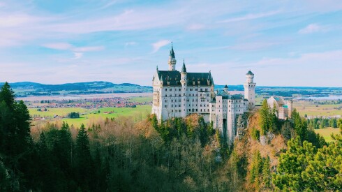 Neuschwanstein Castle in Germany's Bavaria region sits perched high atop a mountain landscape with views of the valley all around