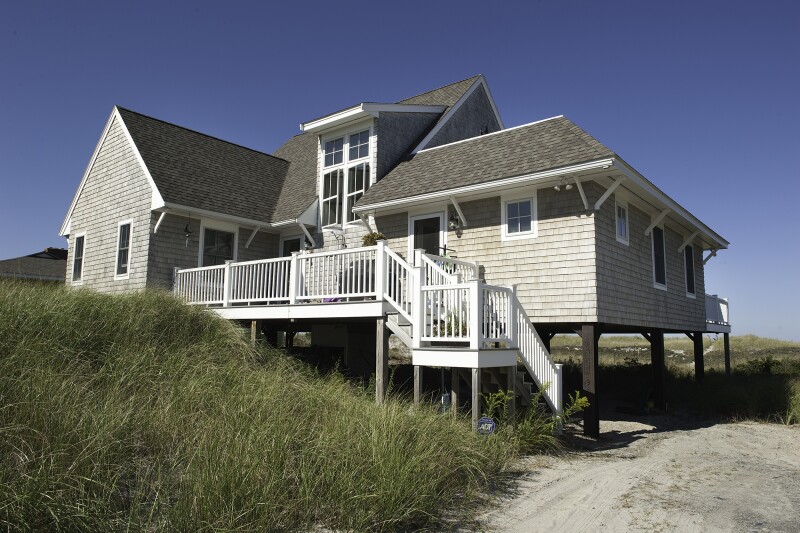 Exterior of large light-gray cottage with white stairs and surrounded by tall grass