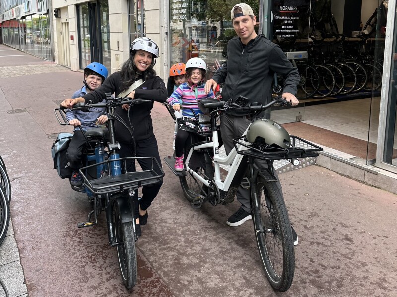 Maddy Novich, her husband, and their three kids pose with two cargo bikes on sidewalk