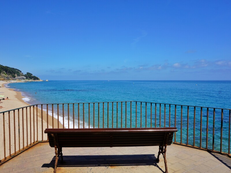 Empty brown bench overlooking a stretch of sand near the beach of Sant Pol de Mar
