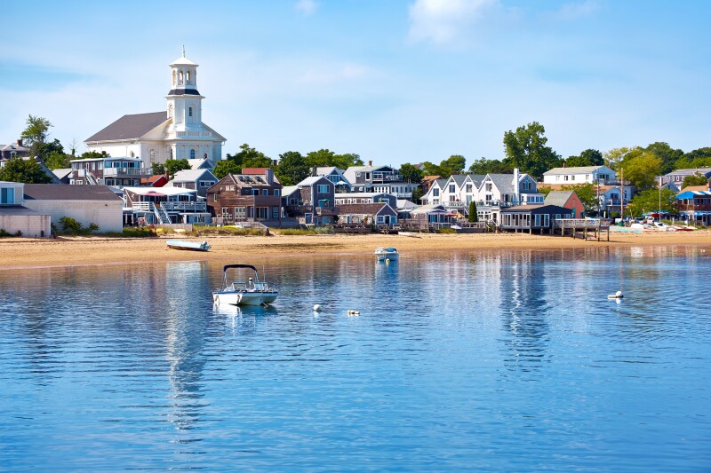 Calm water and shore of Provincetown beach, with small white buildings in background