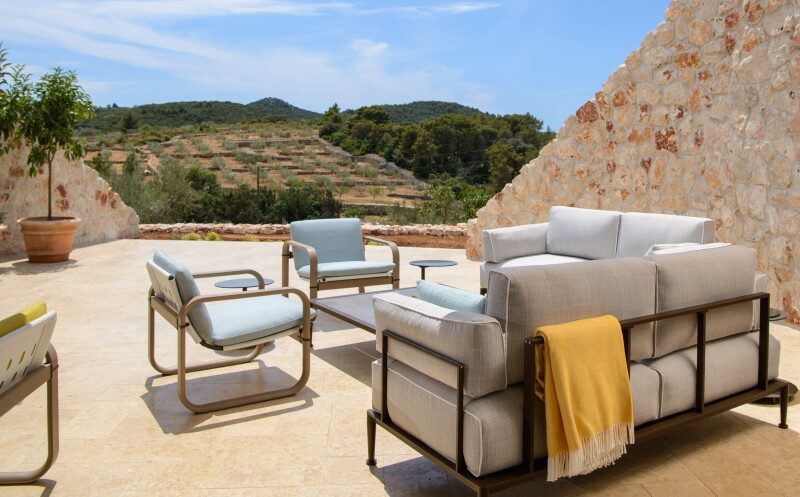 Cushioned chairs and sofa in pastel colors outdoors at Villa Nai 3.3 Hotel, with view of green lands and trees in distance