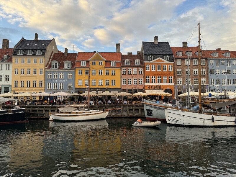 Colorful buildings in hues of yellow, pink, blue, orange, and brown line the Nyhavn canal in Copenhagen, which is lined with restaurant umbrellas and docked sailboats
